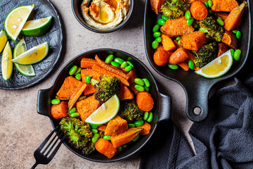 Baked vegetables in cast iron pans, dark background, top view. Baked sweet potatoes, broccoli, carrots, and beans.