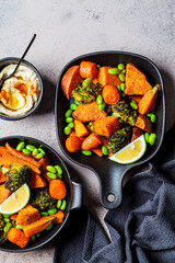 Baked vegetables in cast iron pans, dark background, top view. Baked sweet potatoes, broccoli, carrots, and beans.