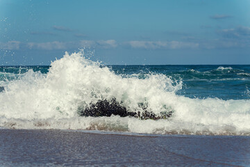 Waves crashing into a rock in the sea with power and making white foam Selective focus