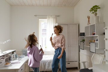 Excited Caucasian mother and teenage daughter have fun sign listen to music on weekend at home...