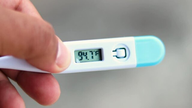 Fever Concept. Man holds digital thermometer closeup. The temperature reading on the thermometer rises in Fahrenheit.