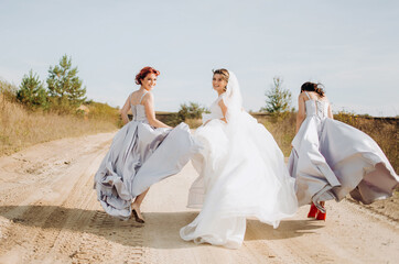 Fototapeta na wymiar Crazy bride in a wedding dress and her bridesmaids run along the sandy path.