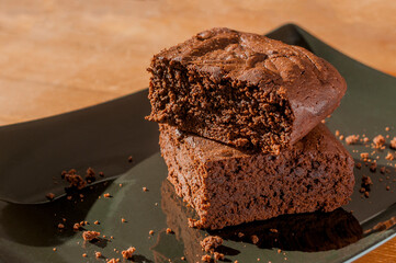 Two slices of chocolate brownies on a black plate on wooden table