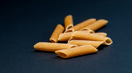 Traditional Italian pasta on black background. Wholegrain raw uncooked macaroni.