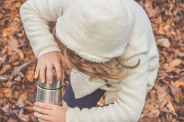 a autumn day child with a thermos on the background of fallen leaves