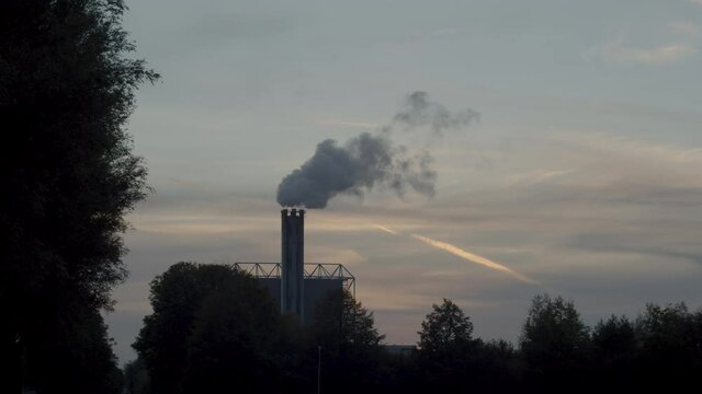Polluting smoking factory chimney against a sunset