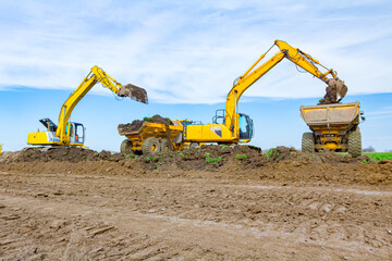 Big excavators are loading two trucks with ground on building site