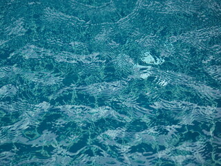 Rain drops falling blue water in pool background ripples on the surface texture, glittering bokeh abstract