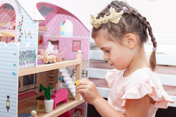 Beautiful little girl in pink dress plays with a doll's house