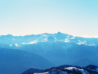 View of a blue snowy mountain valley with woodland below and a clear sky background