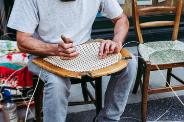 Close up sur les mains d'un artisan rempailleur de chaise en train de réparer une chaise en osier