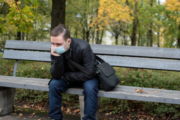 young adult guy sits on a park bench in dark clothes, green park autumn