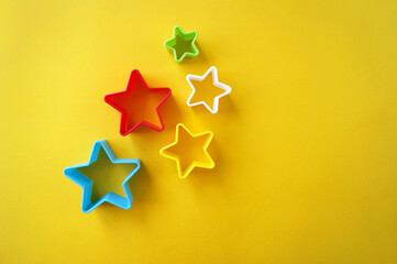 Plastic molds of multi colors for making cookies in the shape of a star on a yellow background.