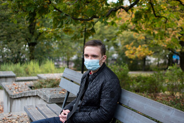 Fototapeta premium young adult guy sits on a park bench in dark clothes, green park autumn