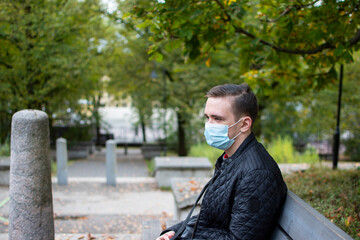 Obraz premium young adult guy sits on a park bench in dark clothes, green park autumn