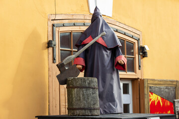 Medieval executioner in a cloak with a hood and a chopping block with an ax on the platform.