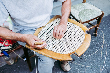 Close up sur les mains d'un artisan rempailleur de chaise en train de réparer une chaise en osier