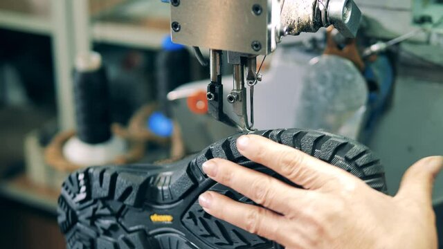 Shoemaker attaching sole to a shoe at a footwear facility. Close up