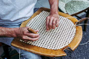 Close up sur les mains d'un artisan rempailleur de chaise en train de réparer une chaise en osier