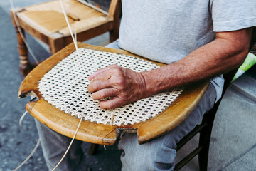 Close up sur les mains d'un artisan rempailleur de chaise en train de réparer une chaise en osier