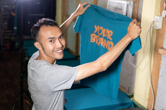 male workers smile confidently holding the results of printing T-shirts at the workshop.