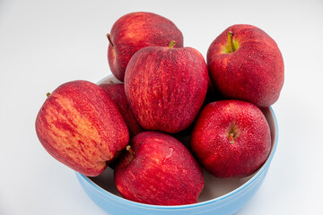 Pile of red apple in blue bowl with clear water drop on 
shell surface texture pattern isolated, white background