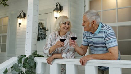Senior elderly Caucasian couple drinking wine in porch at home. Happy mature retired family resting
