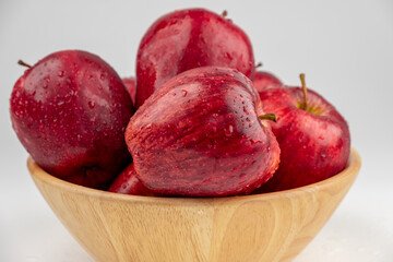 Pile of red apple in wooden bowl with clear water drop on 
shell surface texture pattern isolated, white background