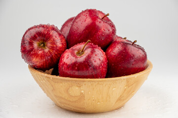 Pile of red apple in wooden bowl with clear water drop on 
shell surface texture pattern isolated, white background