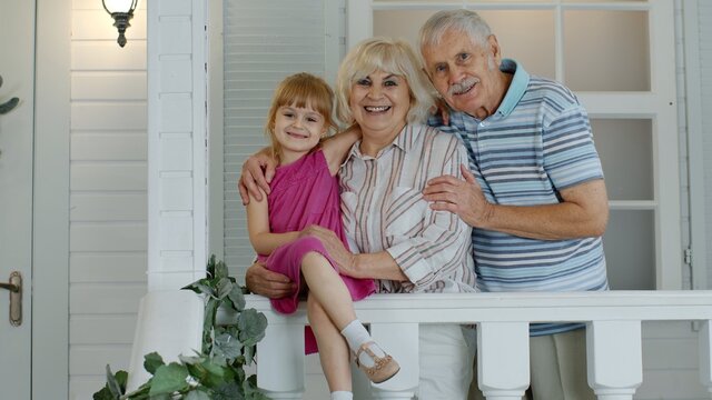 Senior Grandfather And Grandmother Couple With Granddaughter Waving Hand, Smiling, Saying Hello