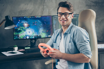 Portrait of his he nice attractive cheerful guy geek playing web network videogame spending free time sitting in chair at modern industrial interior loft concrete wall style work place station