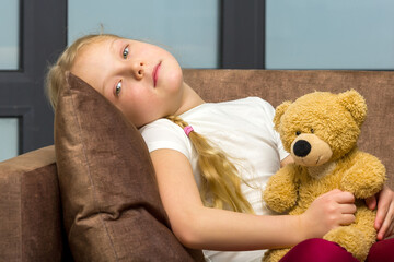 Little girl on sofa hugging teddy bear.