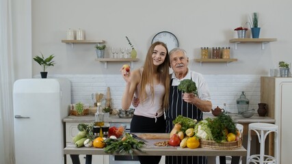 Mature man with grandchild girl recommending eating raw vegetable food. World vegan day concept