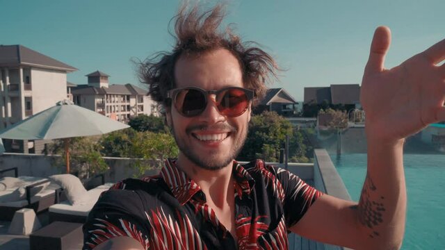 POV of handsome man waving hand in greeting saying hello to smartphone making video call on holiday in exotic country