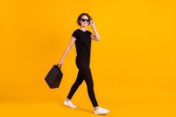 Full length body size profile side view of nice trendy cheerful girl walking carrying bags isolated bright yellow color background