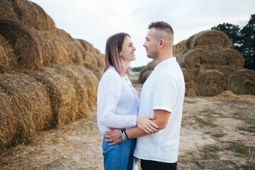 Lovers walk on a farm. A man and a woman are standing near haystacks. People are standing near haystacks. Farm.
