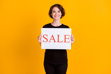 Portrait of attractive cheerful girl holding in hand paper placard sale advert isolated over bright...