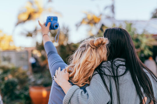 Two Femaile Freinds Taking Selfie Photo With Instant Camera, Back View