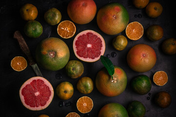 Low key top view of citrus fruits background. Mix of cutted grapefruits and mandarins. Flatlay composition with selective focus