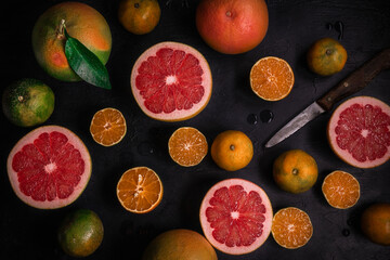 Low key top view of citrus fruits background. Mix of cutted grapefruits and mandarins. Flatlay composition with selective focus
