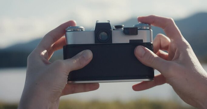 Female hands take photo with analog camera at lake outdoors close up