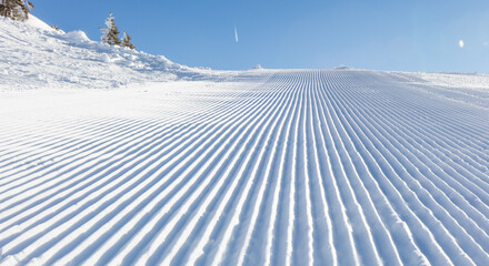 Close-up straight line rows of freshly prepared groomed ski slope piste.
