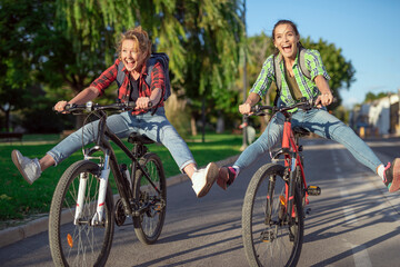 Fototapeta premium Two pretty young caucasian girls having fun on bicycles along the street. Best friends enjoying a day on bikes. Sunny summer evening