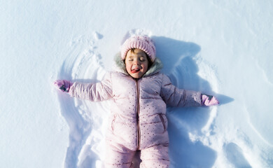 Top view portrait of cheerful small girl lying in snow in winter nature, making angels.