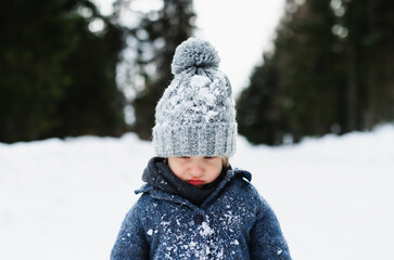 Front view of unhappy small child standing in snow, holiday in winter nature.