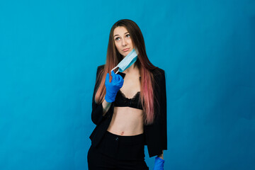 Cheerful and joyful young female with protective medical mask and gloves on blue background.