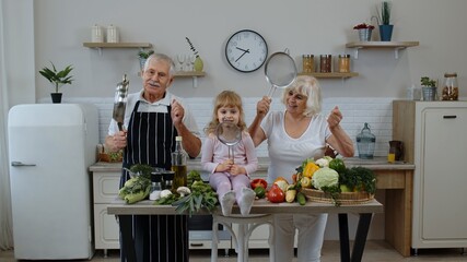 Senior woman and man with grandchild girl making a funny dance with strainer and vegetables at home