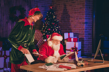 Photo portrait of santa claus and elf reading letters from kids