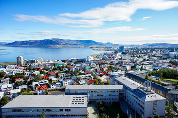 Colored roofs of houses in Rekjavik against the background of blue sky and a large mountain. Iceland - obrazy, fototapety, plakaty
