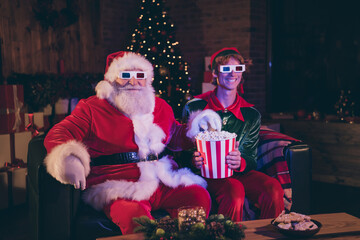 Photo portrait of santa claus and elf eating popcorn watching movie on sofa in 3d glasses